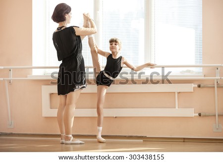 Ballet teacher adjusting leg position of young ballerinas at barre