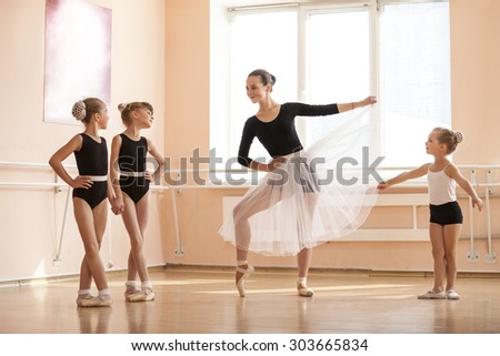 Young girl warming up and talking to younger classmates at ballet dancing class