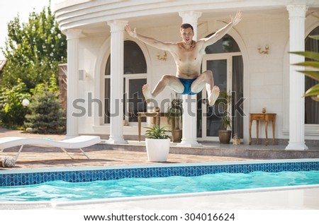 Happy young man jumping into the swimming pool