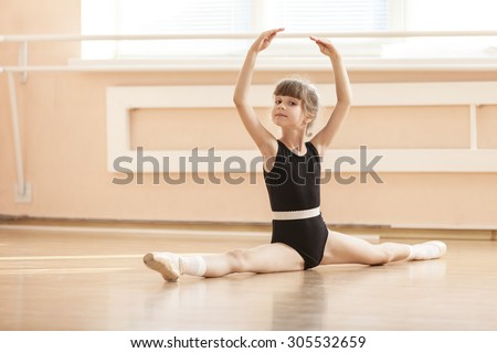 Young girl doing splits while warming up at ballet dance class