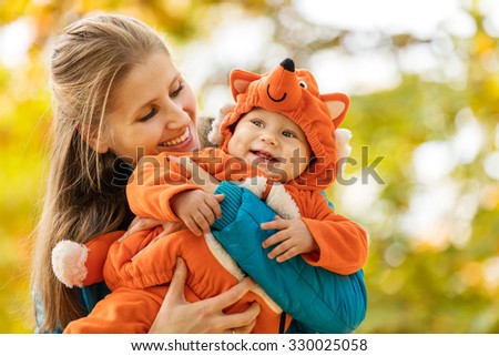 Young woman and her baby son in autumn park, boy dressed in fox costume