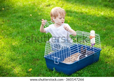 Cute boy opening a cage with a pet rabbit in a park