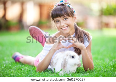 Smiling girl showing a heart sign with her hands over a pet rabbit