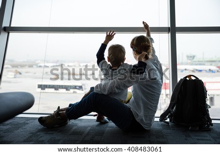 Mother and son sitting near window in airport and waving hands to airplanes