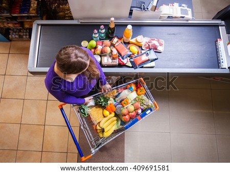 Young woman putting goods from shopping cart on counter for checkout in supermarket