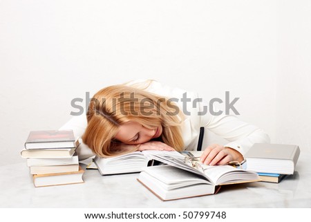 Young woman falling asleep while studying at the table with a lot of books