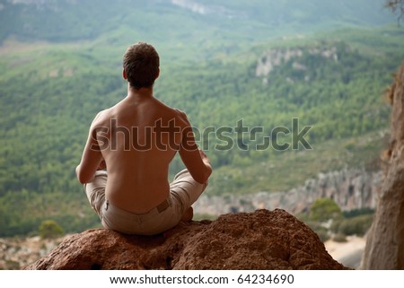 Young muscular man meditating on rock