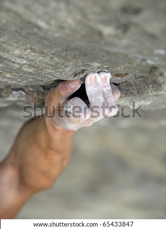 Rock climber\'s hand grasping handhold on natural cliff. His hand is covered in chalk. Shallow depth of field.