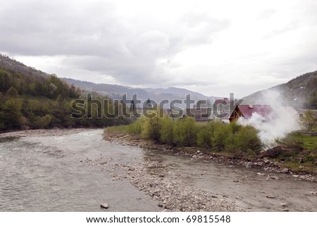 Rural landscape with smoke from the fire on the river bank. A typical view of western Ukrainian countryside, with shallow waters of mountain river on the foreground. Wide angle shot.
