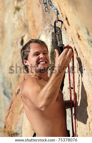 Rock climber struggling fastening rope to quick-draw, image with selective focus