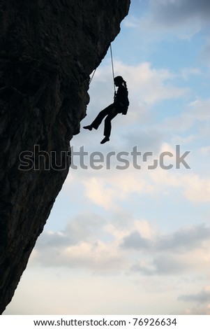 Silhouette of rock climber against cloudy sky background