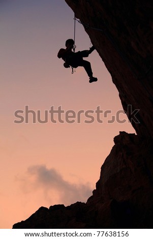 Silhouette of rock climber against sky background at sunset