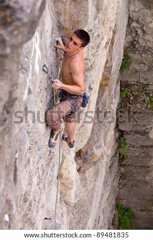 Rock climber fastening rope to quick-draw and looking up at next handhold