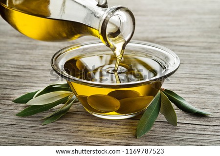 Bottle of Olive oil pouring in a glass bowl with olives