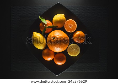 Ripe juicy tangerine, orange mandarin and lemon with leaves on black table