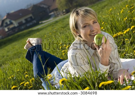 young woman eating apple outside on field