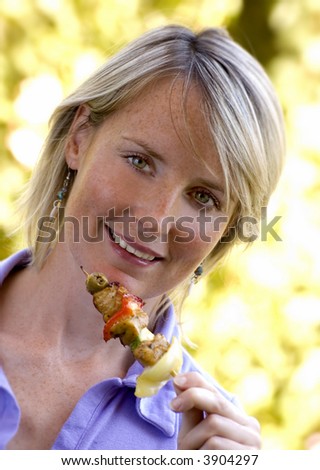 young woman eating chicken on a grill spit portrait