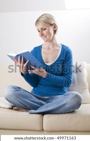 Young blond woman reading a book on the sofa