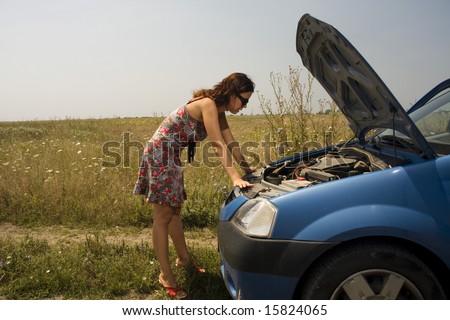 young woman examining the engine of a broken car