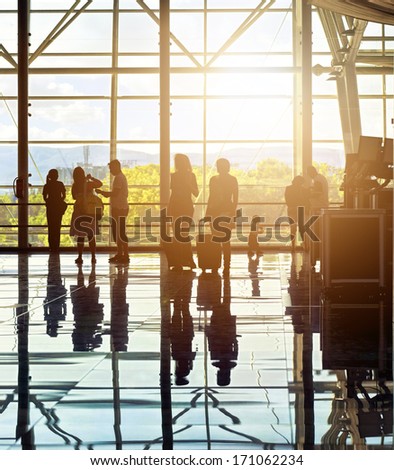 Silhouettes of unrecognizable traveling people at the airport in front of huge window with nature landscape in the background