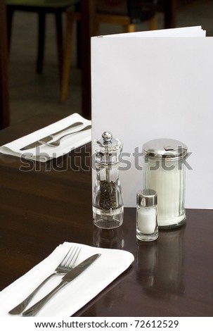 laid table of a fine dining restaurant with menu card, pepper caster and salt shaker.
