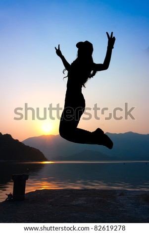 girl jumping with V sign on seaside at beautiful sunset