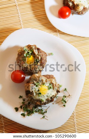 Delicious quail eggs in the minced meat with mushrooms, decorated with cherry tomatoes and broccoli sprouts on white plates.