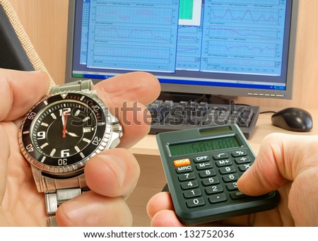 Clock and calculator in hand on the background of the monitor to the schedule on the table and chairs.
