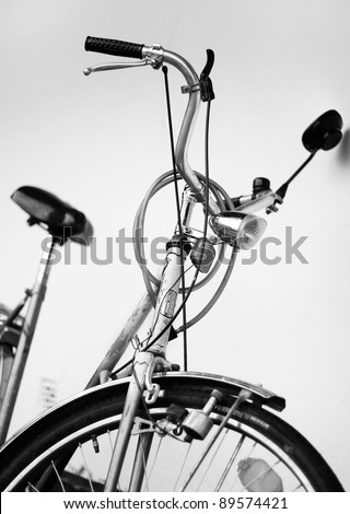 Old retro cruiser bike. Front view. Steering wheel, tire, breaks, seat, mirror and safety lock visible. Black and white.