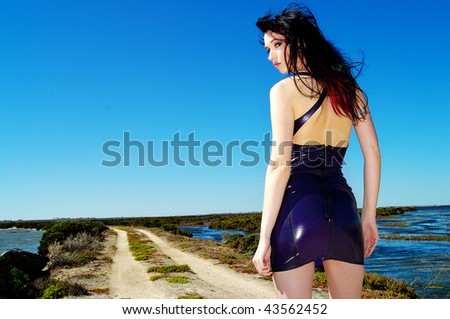 A sexy woman wearing a purple latex dress standing against a bright blue sky