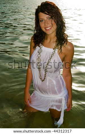 A sexy young woman wearing a wet white dress in the water.