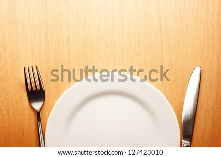 Photo of the fork and knife with white plate on wooden background