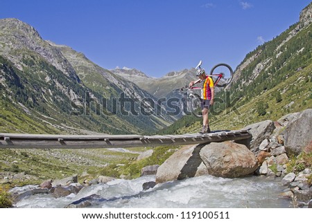 The narrow bridge does not allow riding - mountain biker is shouldering his bike