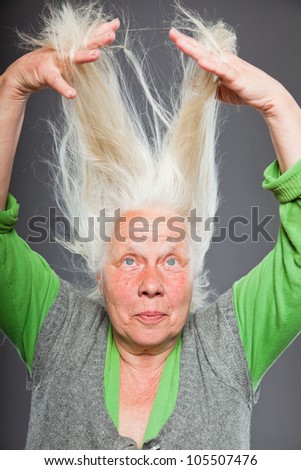Senior woman holding hands in her hair. Spiritual looking. Studio shot isolated on grey background.