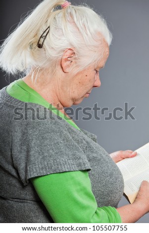 Senior woman white grey hair reading a book. Studio shot isolated on grey background.