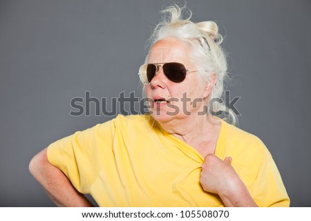 Cool hip senior woman with sunglasses and long grey hair. Expressive face. Studio shot isolated on grey.