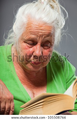 Senior woman sitting chair reading a book. Grey long hair. Studio shot isolated on grey background.