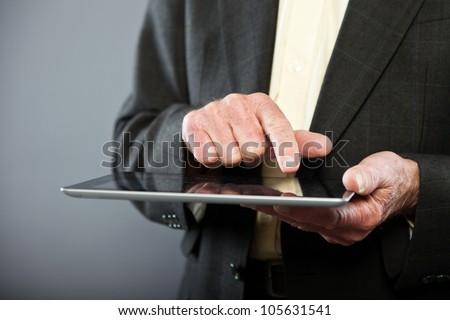Closeup of hand using tablet from senior man in dark suit against grey wall. Well dressed. Studio shot.