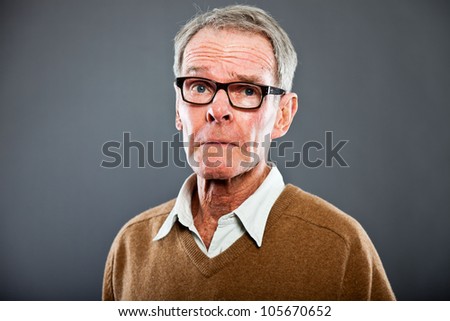 Expressive good looking senior man wearing glasses against grey wall. Funny and characteristic. Well dressed. Studio shot.