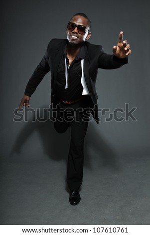 Cool black american man in dark suit. Studio fashion shot isolated on grey background. Wearing dark sunglasses.
