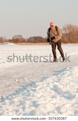 Dutch winter landscape with senior skater on frozen lake. Blue clear sky. Retired man.