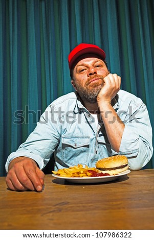 Man with beard eating fast food meal. Enjoying french fries and a hamburger. Trucker with red cap.