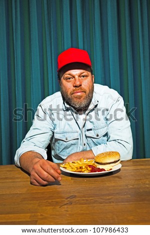 Man with beard eating fast food meal. Enjoying french fries and a hamburger. Trucker with red cap.