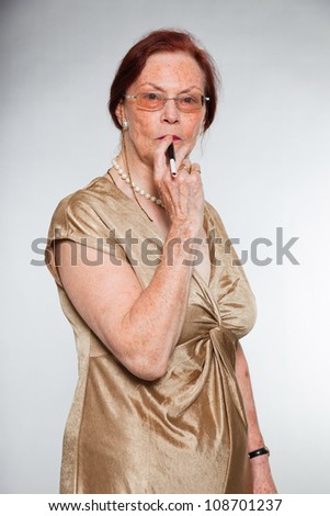 Portrait of good looking senior woman wearing glasses with expressive face showing emotions. Smoking a cigarette. Acting young. Studio shot isolated on grey background.