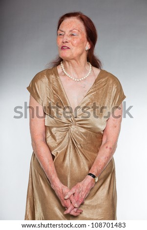 Portrait of good looking senior woman with expressive face showing emotions. Smiling and happy. Acting young. Studio shot isolated on grey background.