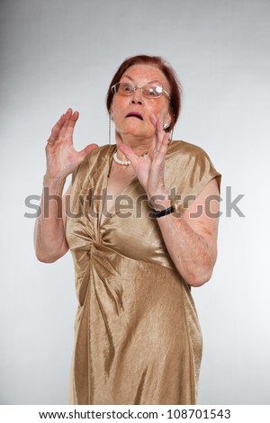Portrait of good looking senior woman wearing glasses with expressive face showing emotions. Scared and frightened. Acting young. Studio shot isolated on grey background.