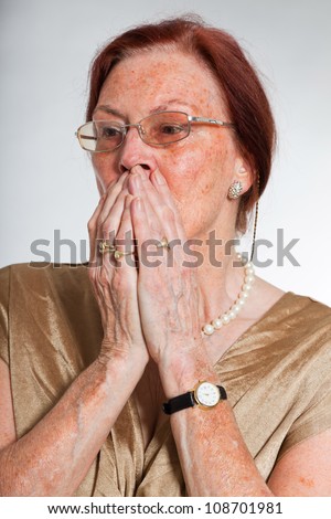 Portrait of good looking senior woman wearing glasses with expressive face showing emotions. Scared and frightened. Acting young. Studio shot isolated on grey background.