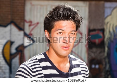 Urban asian man. Good looking. Cool guy. Wearing blue white striped sweater. Standing in front of wooden wall with graffiti.