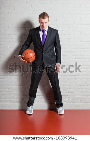 Business man with basketball. Good looking young man with short blond hair. Gym indoor.
