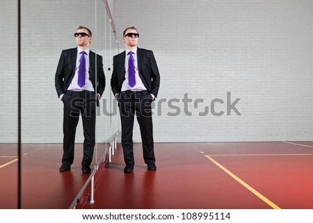Cool good looking business man with dark sunglasses standing against mirror in gym.